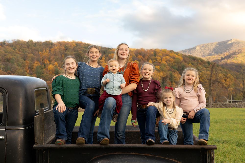Group sitting on vintage truck bed with autumn mountain landscape in background.