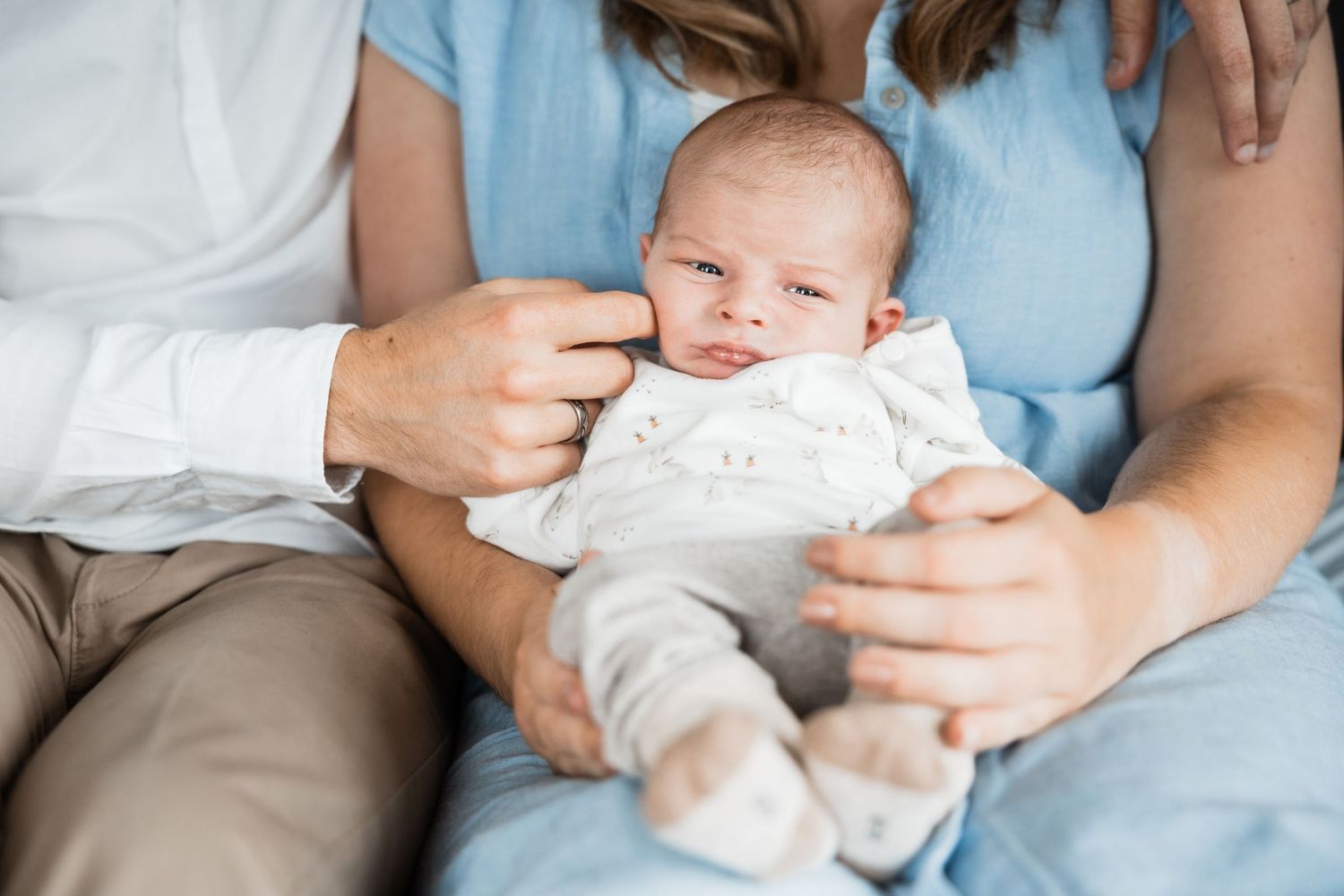 A newborn baby wearing white clothing is held in supporting hands while resting comfortably.