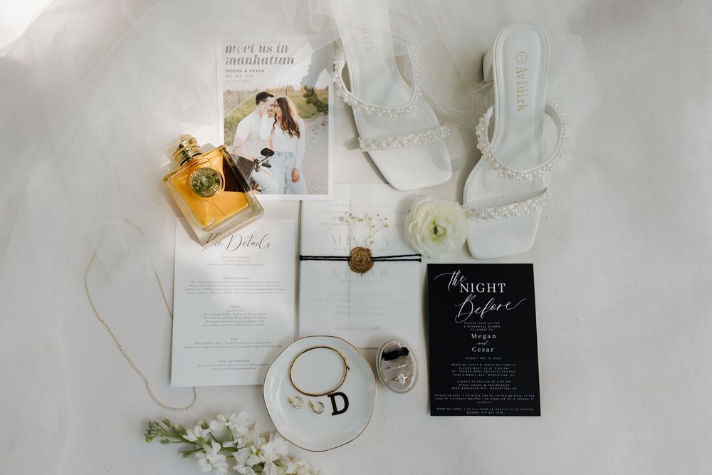 A flat lay wedding photography setup with white and gold invitation suite, bridal heels, rings and delicate floral accents.
