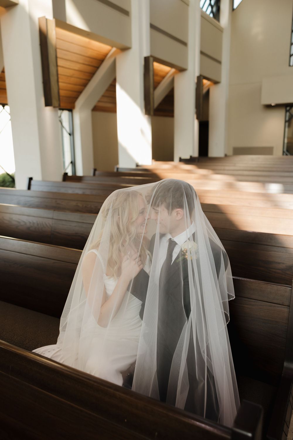 A wedding dress with veil bloom across wooden church pews creating a soft ethereal effect in natural sunlight.