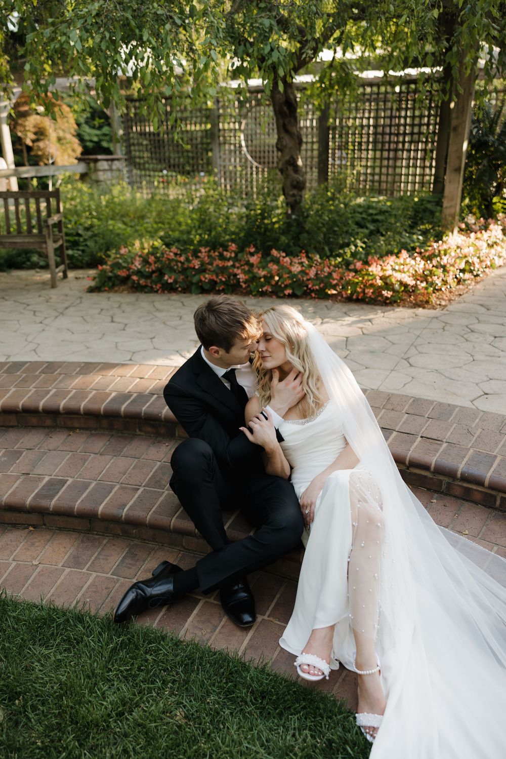 Candid wedding couple sitting on brick steps in a garden setting for romantic photographs.