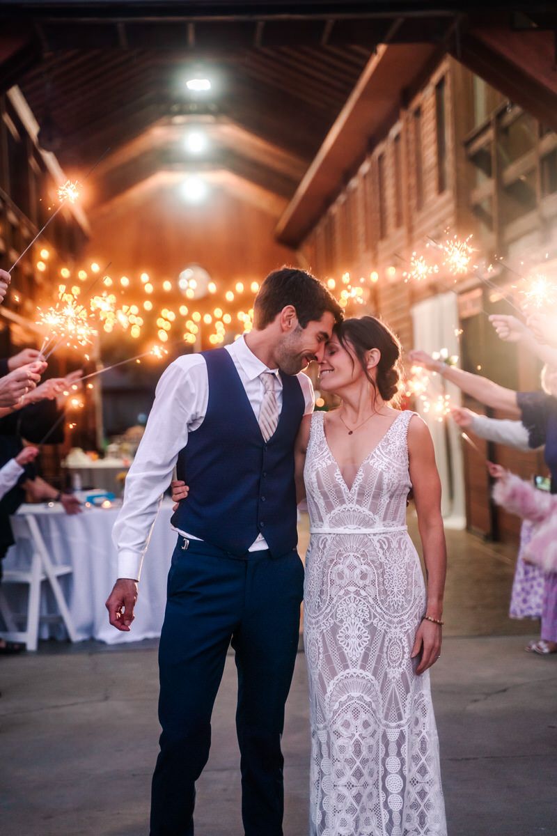 A bride and groom put faces together and smile as guests hold sparklers behind them.