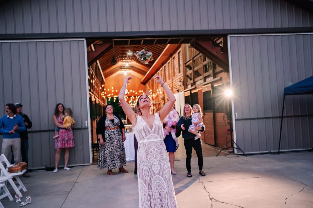 A bride arches as her flowers fly into the air during the flower toss at a backyard DIY wedding reception in West Michigan