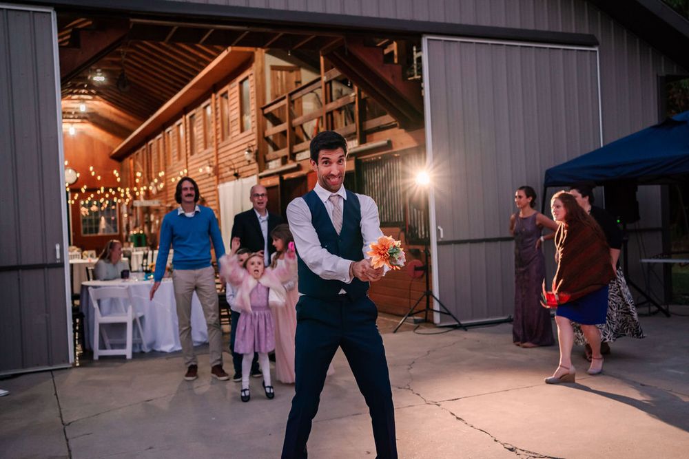 A groom gets ready to throw flowers during the bouquet toss at a back yard DIY wedding in South Haven, Michigan.