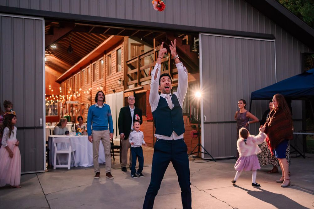 A groom has a bouquet of his own to throw at the end of the wedding night. Guests line up behind him to catch it.