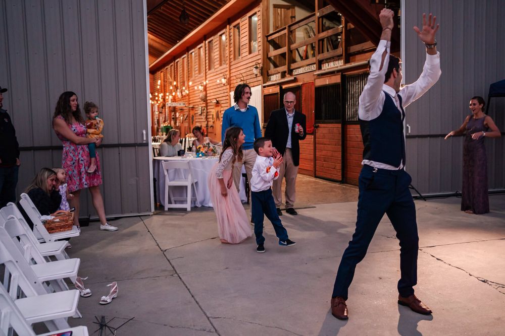 A ring bearer catches a small toss-bouquet thrown by a groom at the end of the night in a small backyard wedding reception.