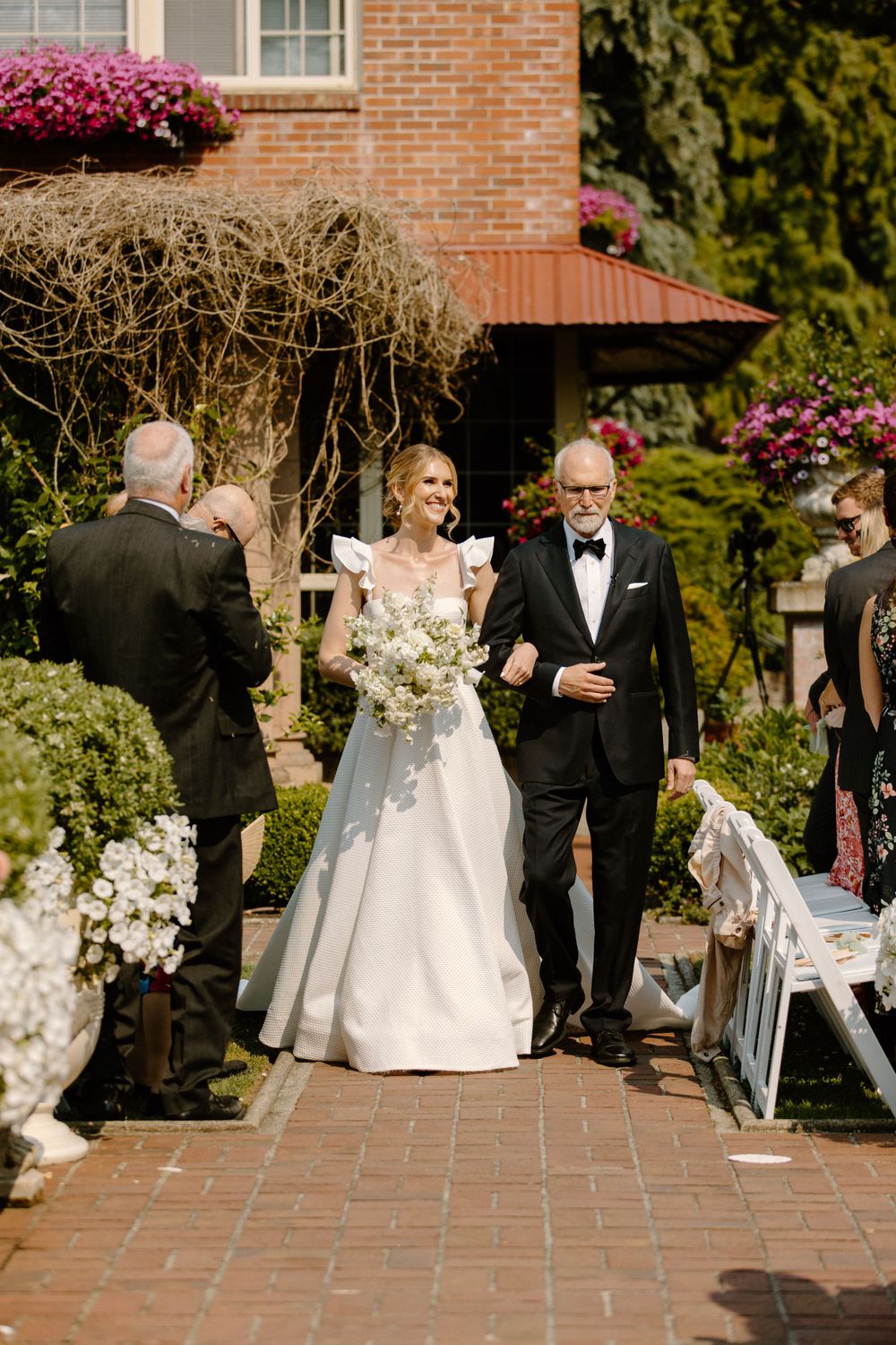 An elegant outdoor wedding ceremony at a brick venue adorned with beautiful pink flowers and greenery.
