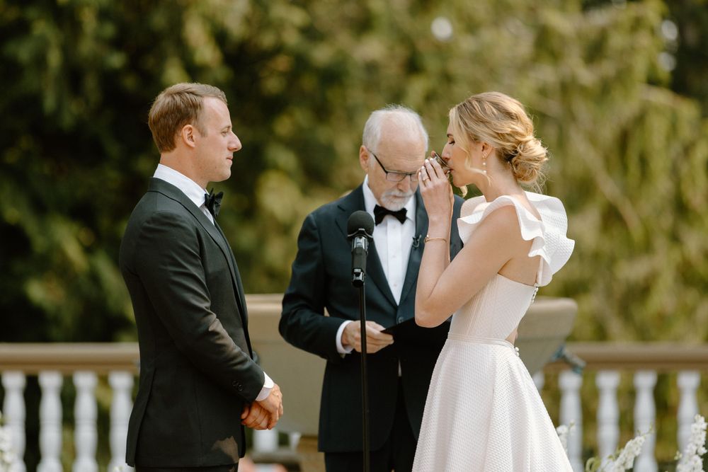 A couple shares a moment during their outdoor wedding ceremony with an officiant on a white porch.