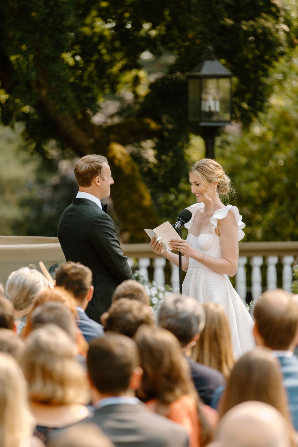 A couple exchanges vows during an outdoor wedding ceremony as guests look on from their seats.