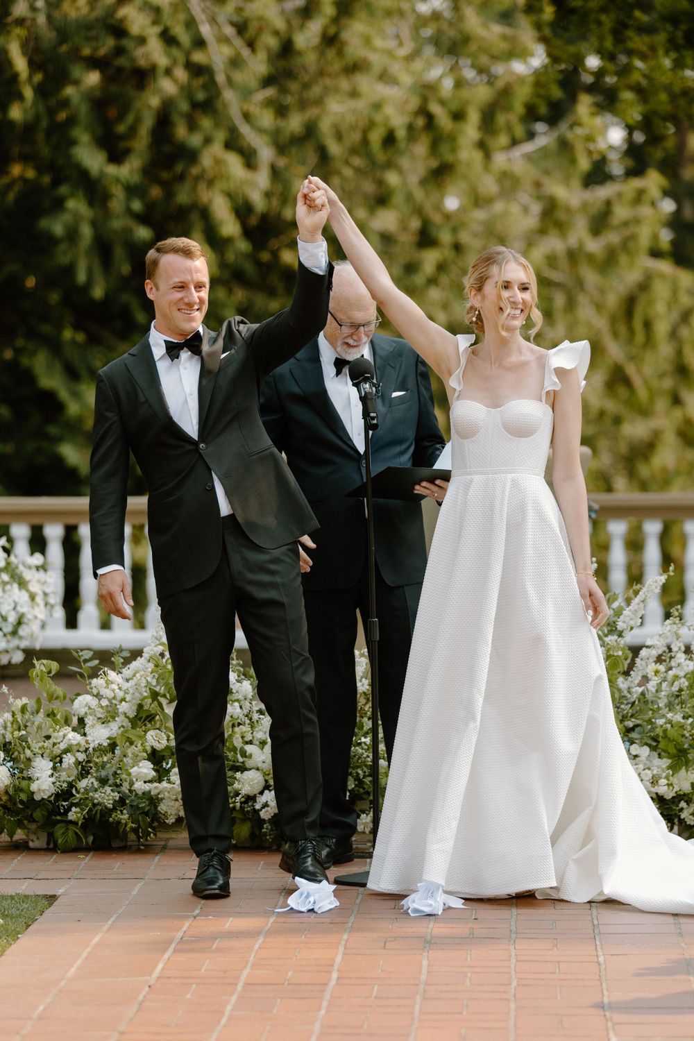 A wedding ceremony on a terrace with newlyweds in formal attire raising joined hands in celebration.