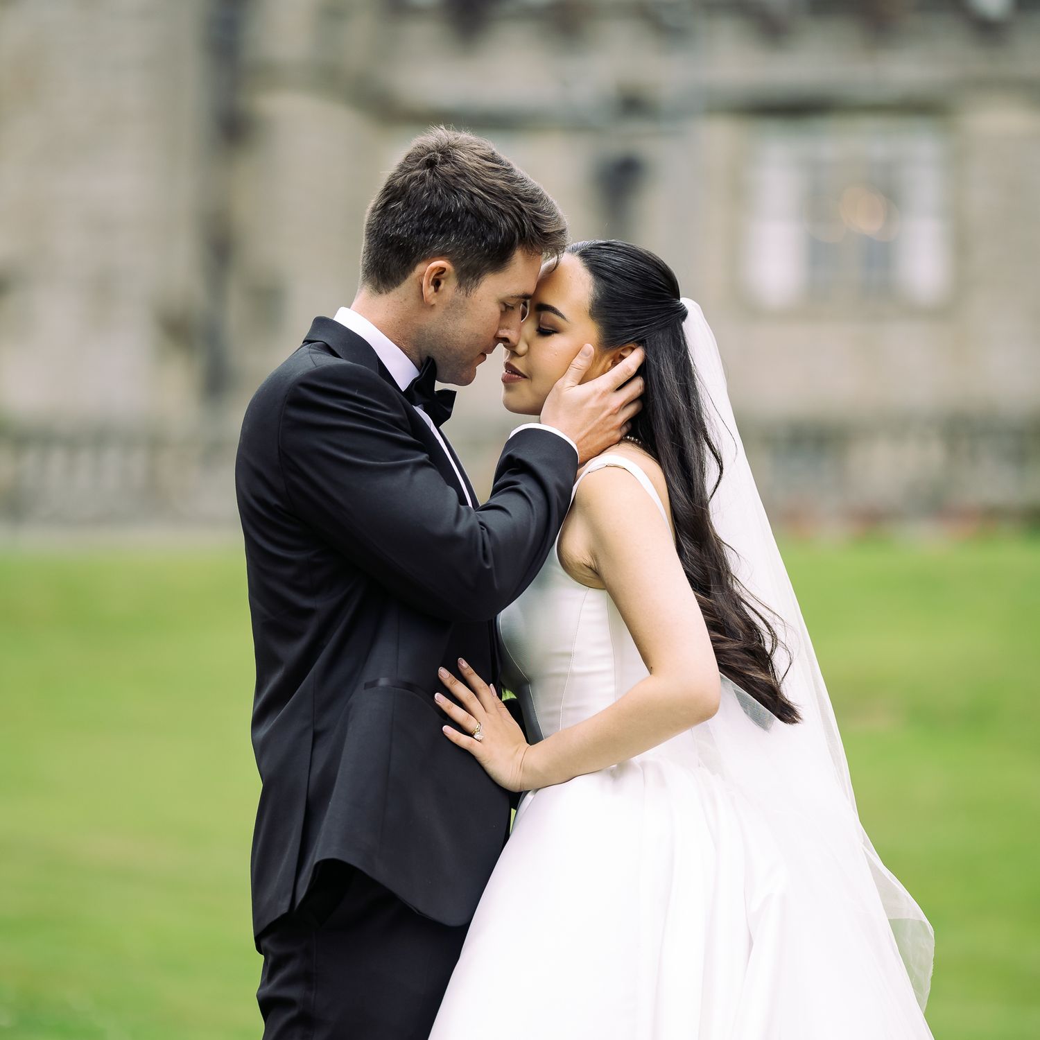 A romantic wedding moment between a couple in traditional attire sharing an intimate embrace outdoors on the grass.