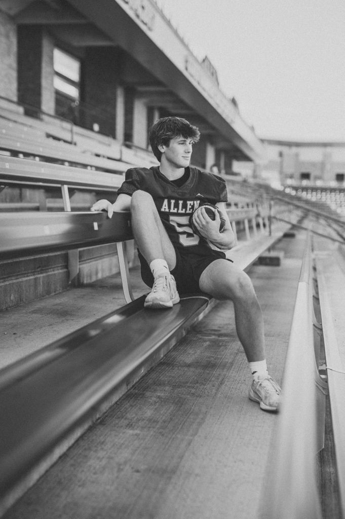 Black and white sports photo of a basketball player sitting alone in empty stadium bleachers wearing Allen jersey.