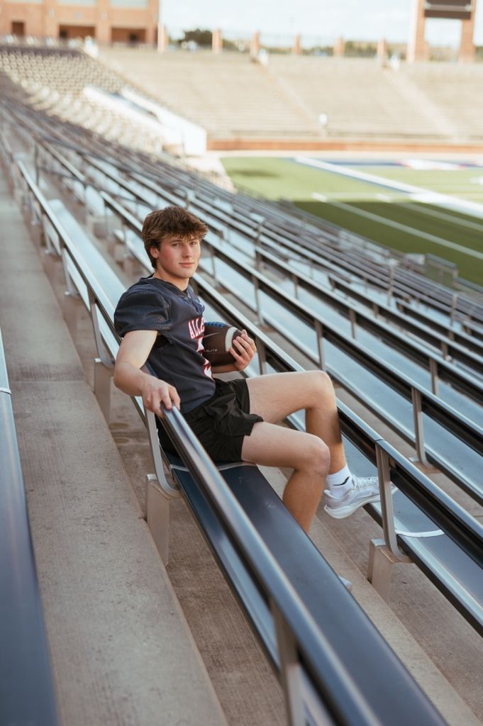 A young person rests on stadium bleachers while holding a football and wearing athletic attire.