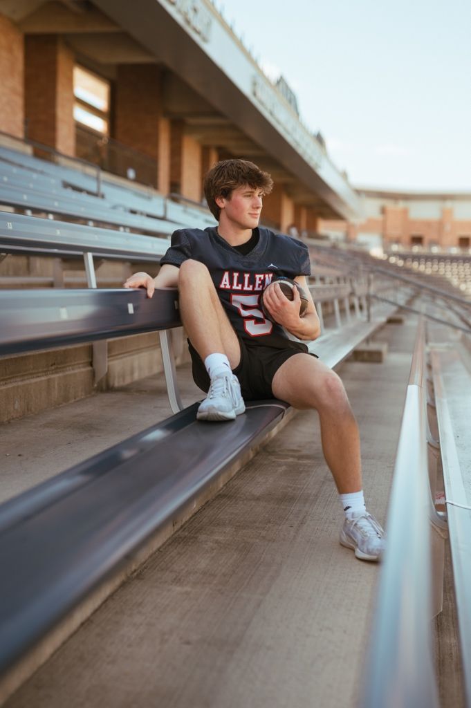 Student athlete in black uniform sits on stadium bleachers during outdoor photo session.