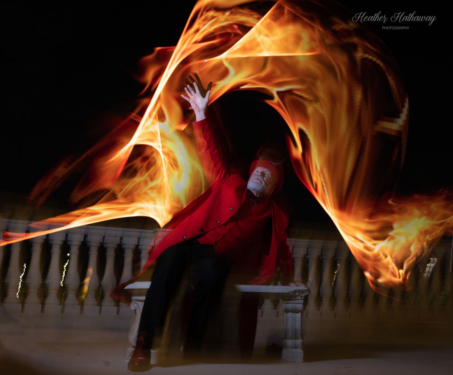 A ballet dancer in a red dress creates flowing motion trails of fire and light against a dark background.