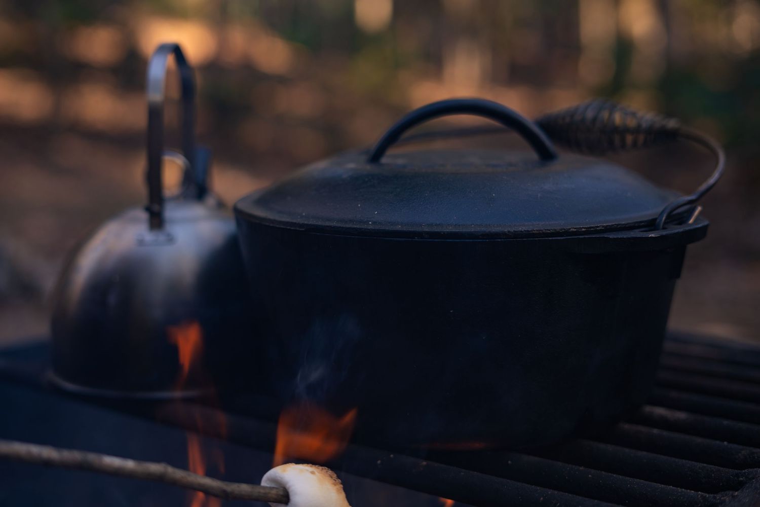 Lodge Dutch oven and stainless steel kettle over an open fire, perfect for outdoor cooking and campfire meals.