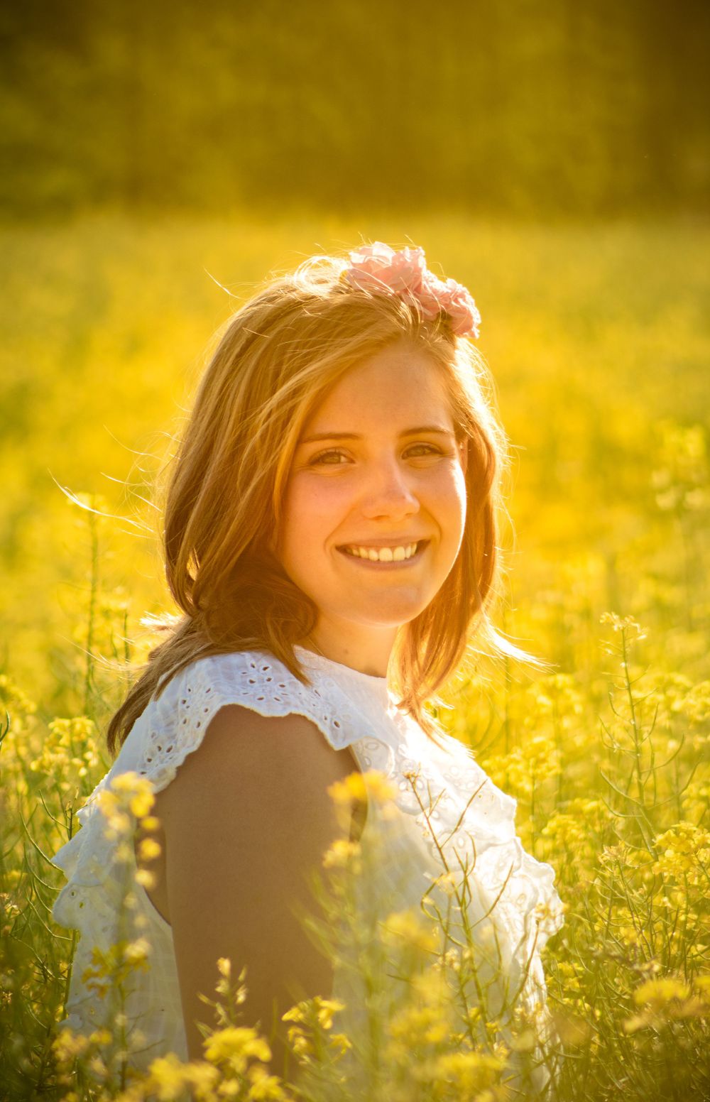 A person in a white lace dress sits in a sunlit meadow of yellow wildflowers at golden hour.