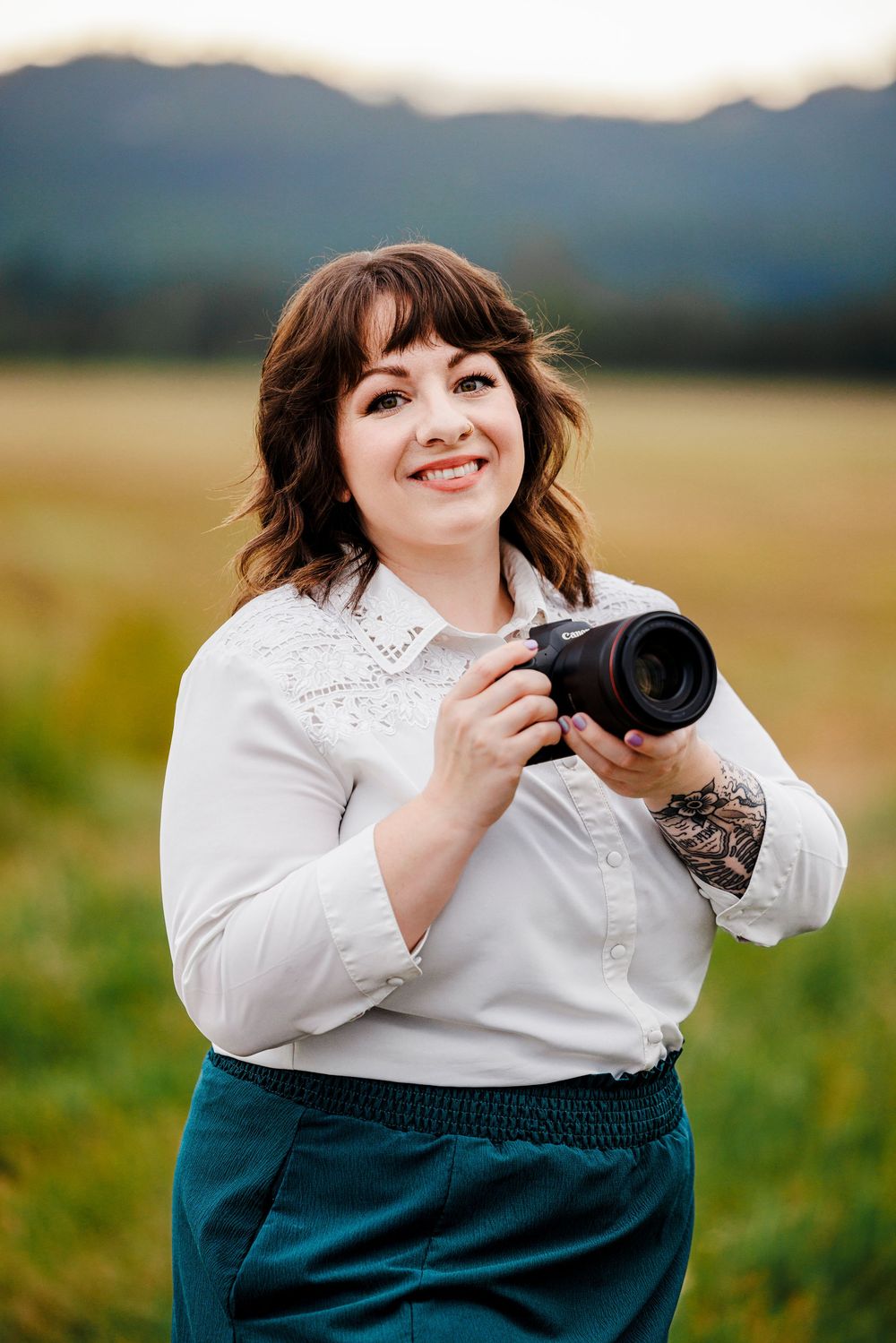 Professional photographer in black blazer, ripped jeans and combat boots poses energetically with camera against white backdrop.