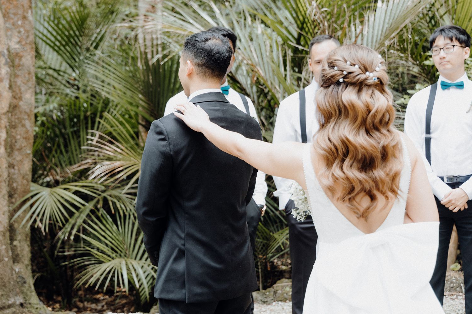 A bride in a white dress reaches out to touch the groom for their First Look captured by Apertured Media Auckland Wedding Photographer.