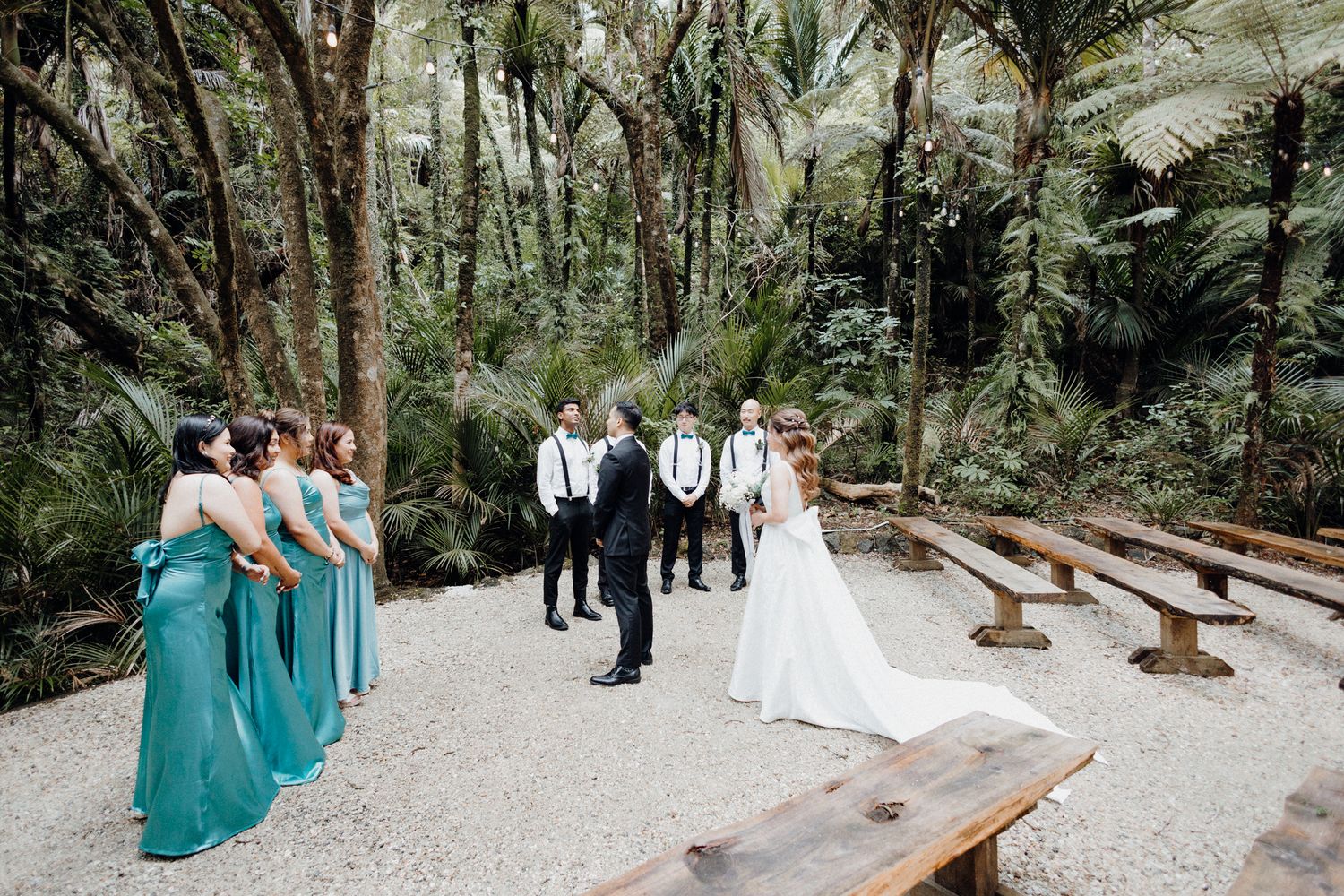 A First Look taking place in a lush forest garden with wooden benches captured by Apertured Media Auckland Wedding Photographer.