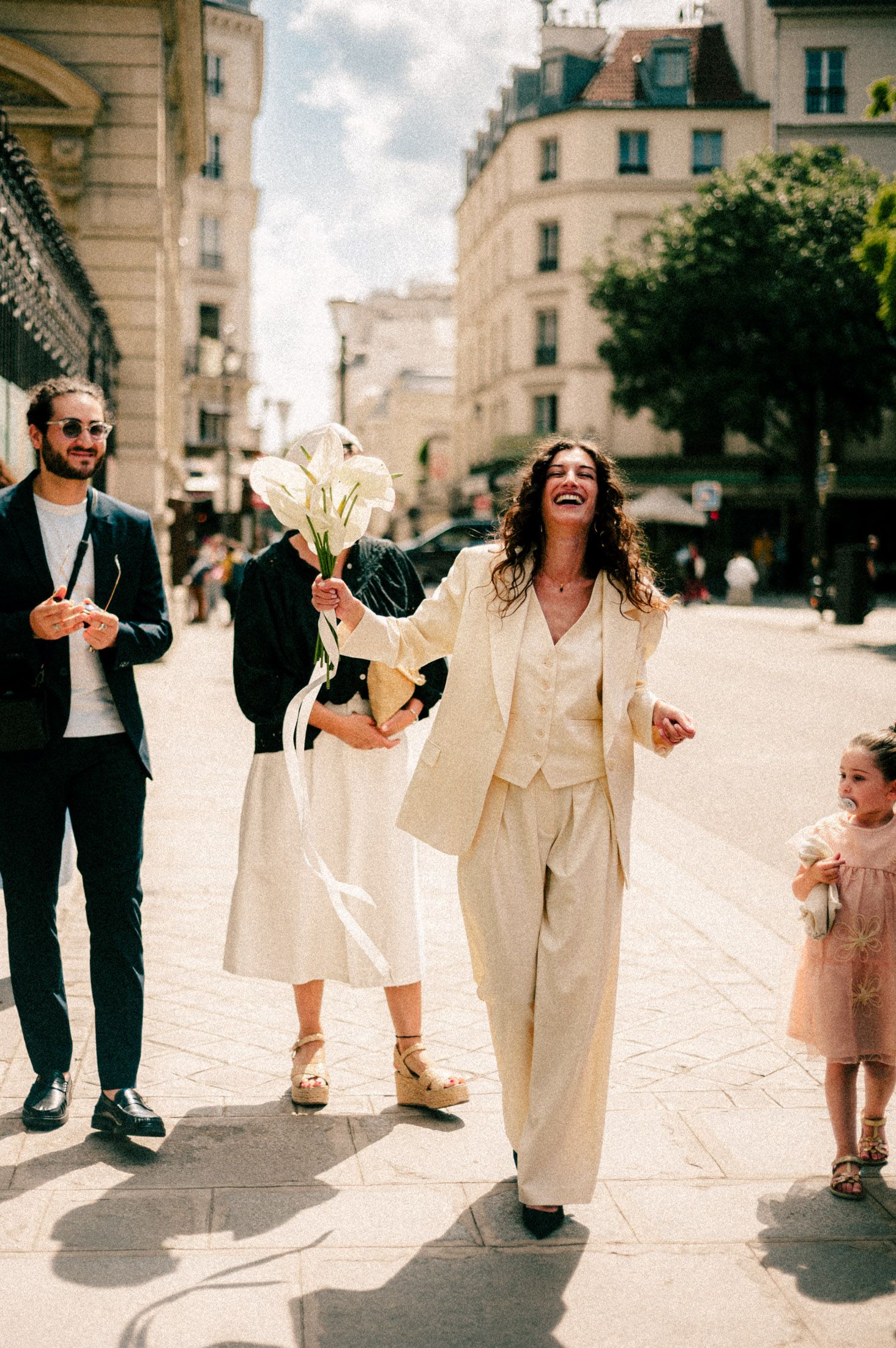 A joyful group walking down a charming Parisian street in light-colored outfits on a sunny day.