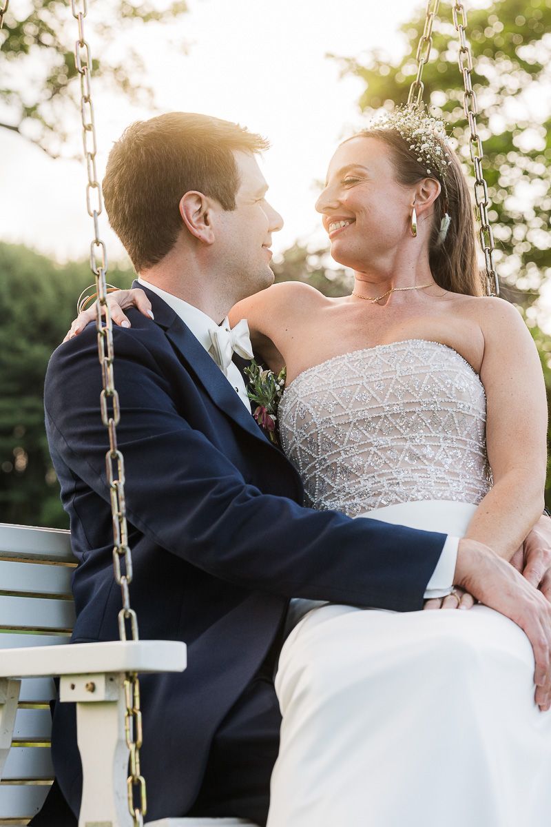 Newlywed couple sit on a swing at Shady Elms Farm Pittsburgh Pennsylvania posing for photos for photographer and videographer at sunset.