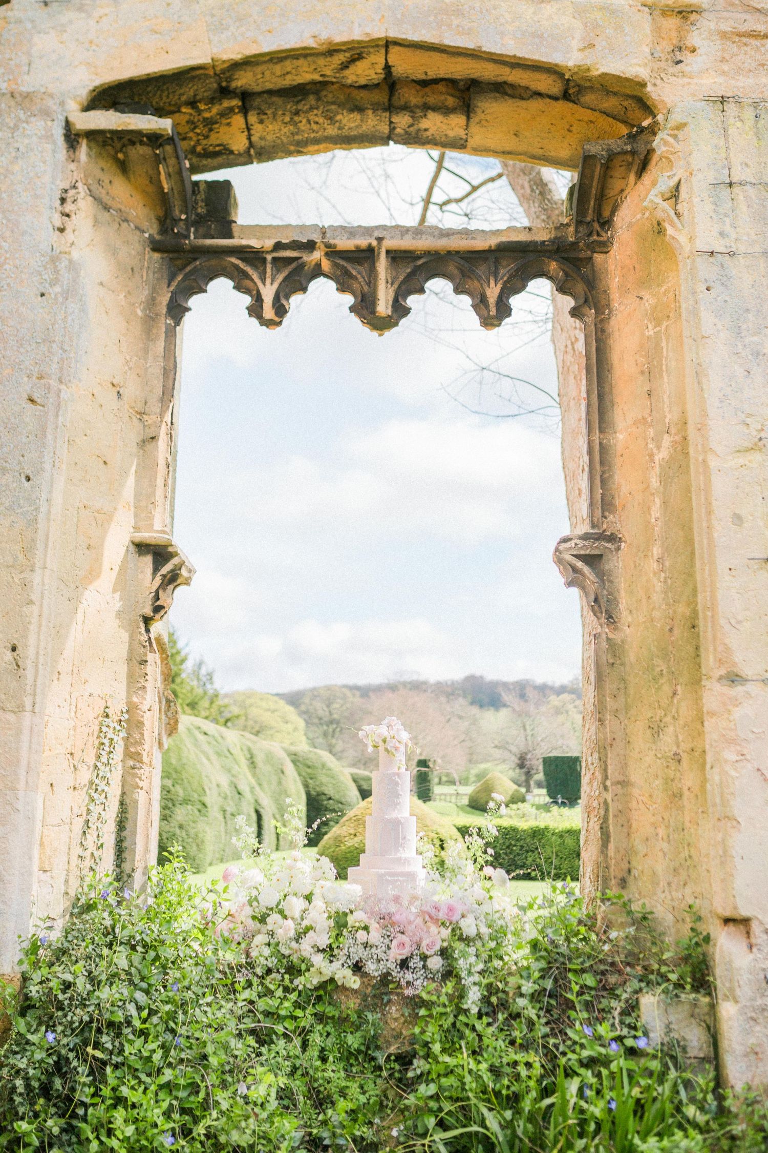 Stone archway frames a serene garden view with feature cake at a Sudeley Castle Wedding by Hayley Elizabeth Photography