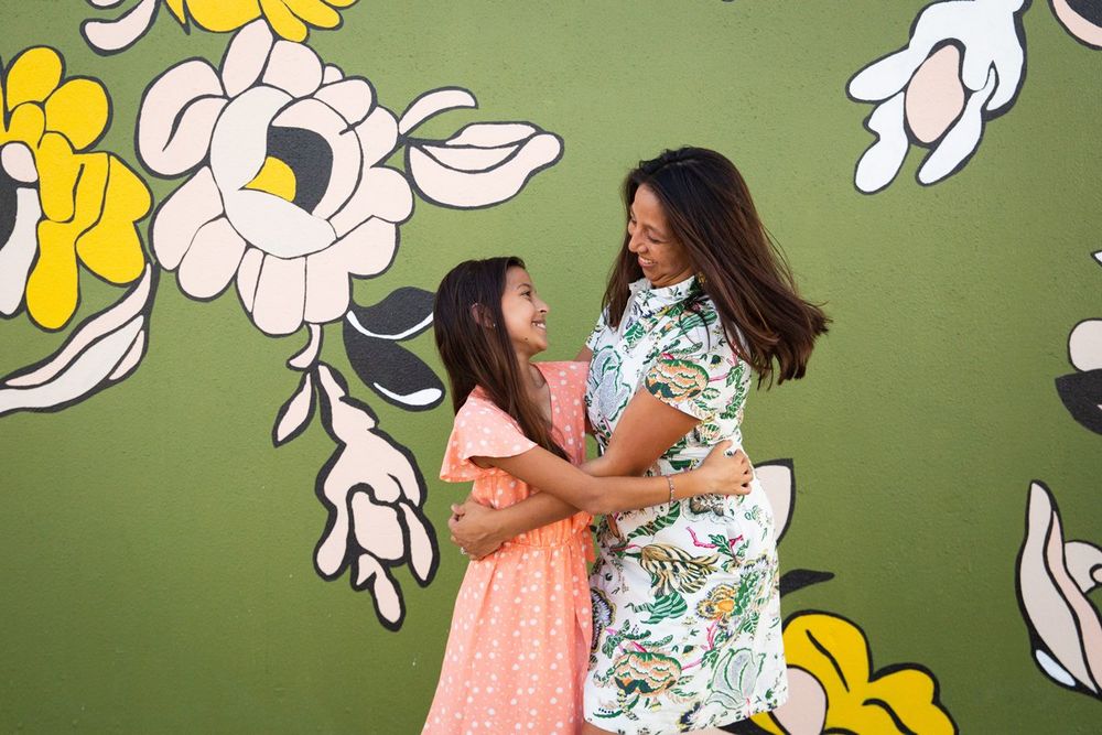 Two people share a joyful moment together in front of a green wall decorated with large floral art elements.