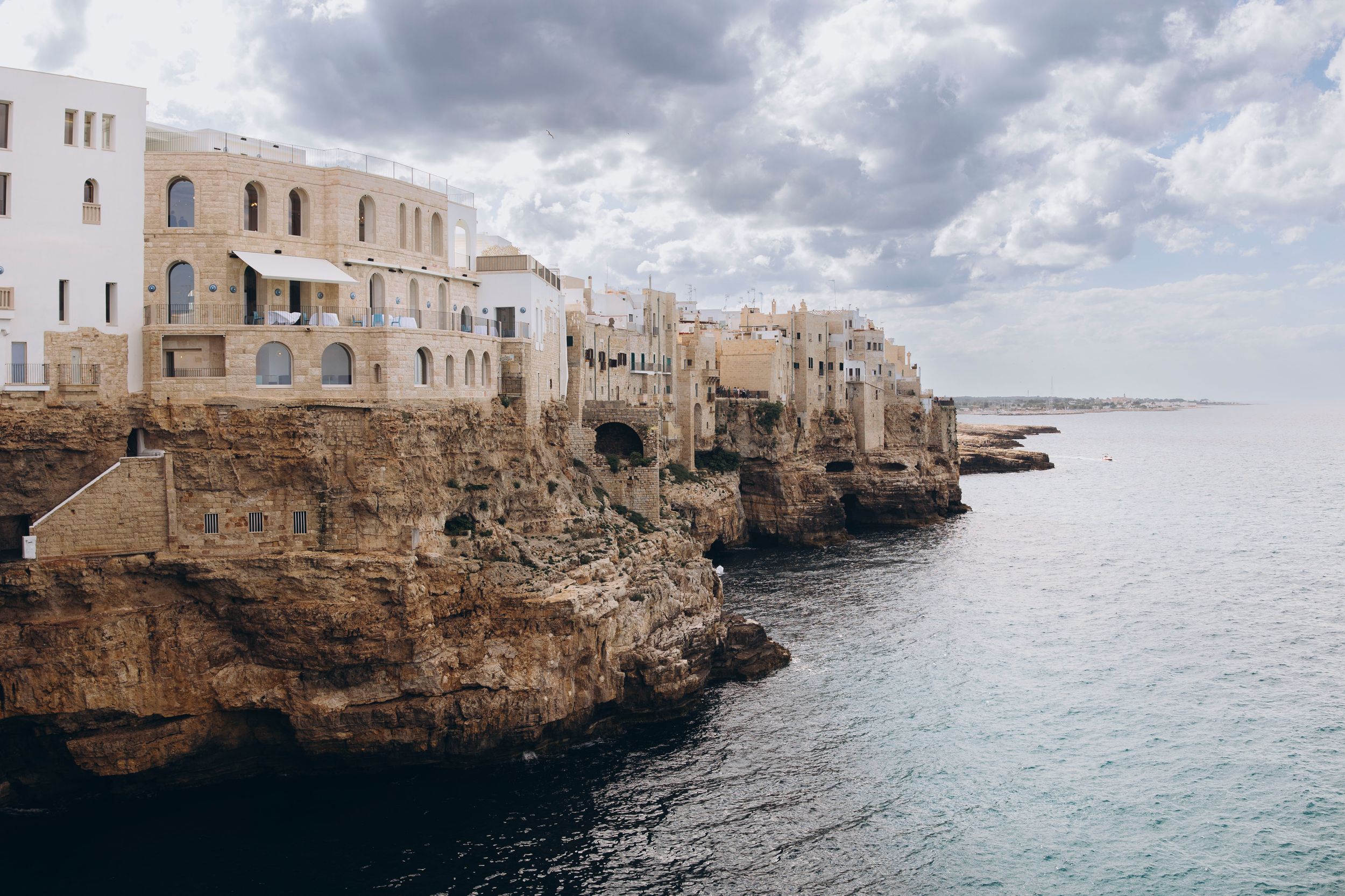 Historic white buildings perch on dramatic limestone cliffs overlooking the turquoise Mediterranean Sea in Polignano a Mare, Italy.