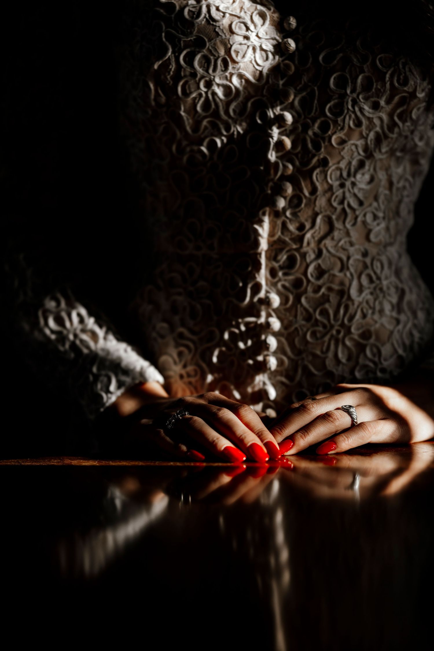Hand with red manicured nails reaching for fresh strawberries in crystal cocktail glasses on white tablecloth.