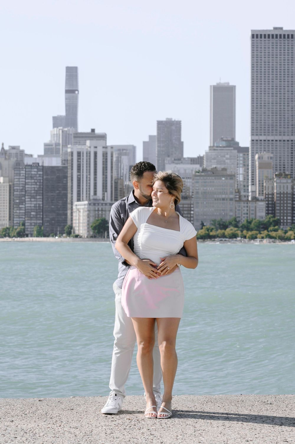 A romantic couple embraces along Lake Michigan with the iconic Chicago skyline rising behind them.