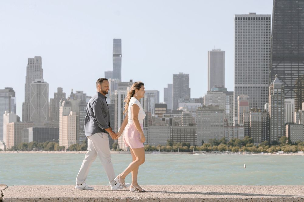 A couple strolls along Lake Michigan with the Chicago skyline creating a stunning urban backdrop on a sunny day.
