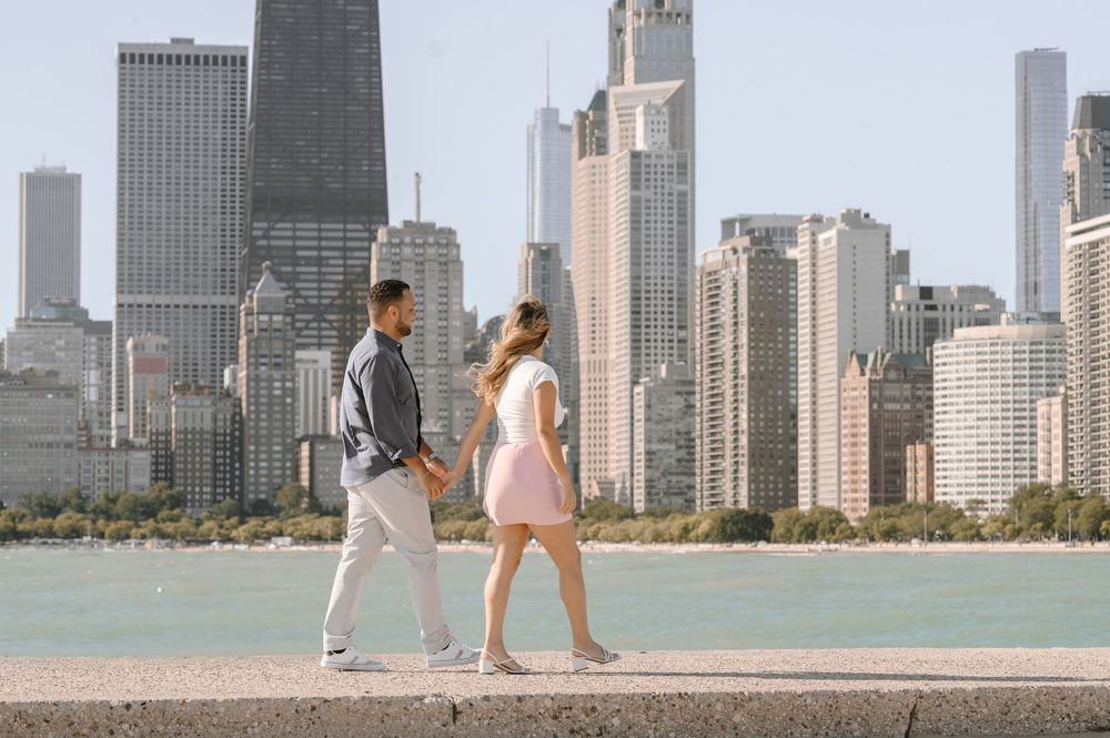 Two people walking along Lake Michigan with the iconic Chicago skyline backdrop on a sunny day.