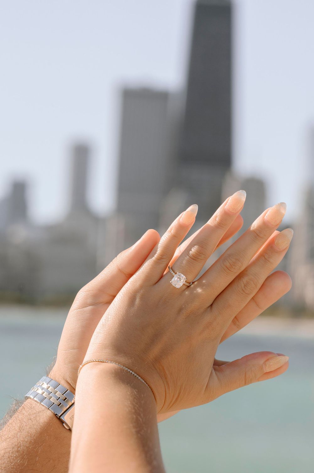 Engagement ring displayed on hand with Chicago's John Hancock building visible in background.