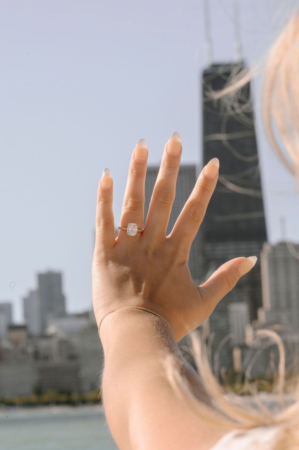 Close-up of engagement ring with Chicago cityscape and Lake Michigan visible behind.