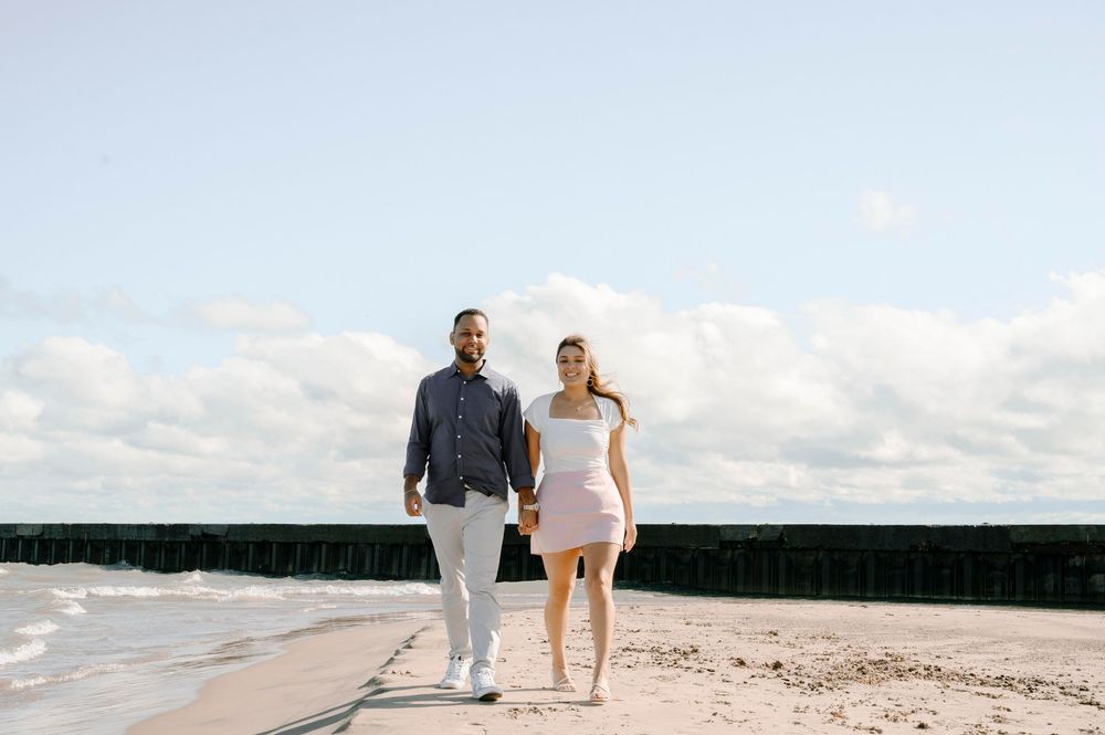 A couple walking hand in hand along a scenic beach walkway under cloudy skies.