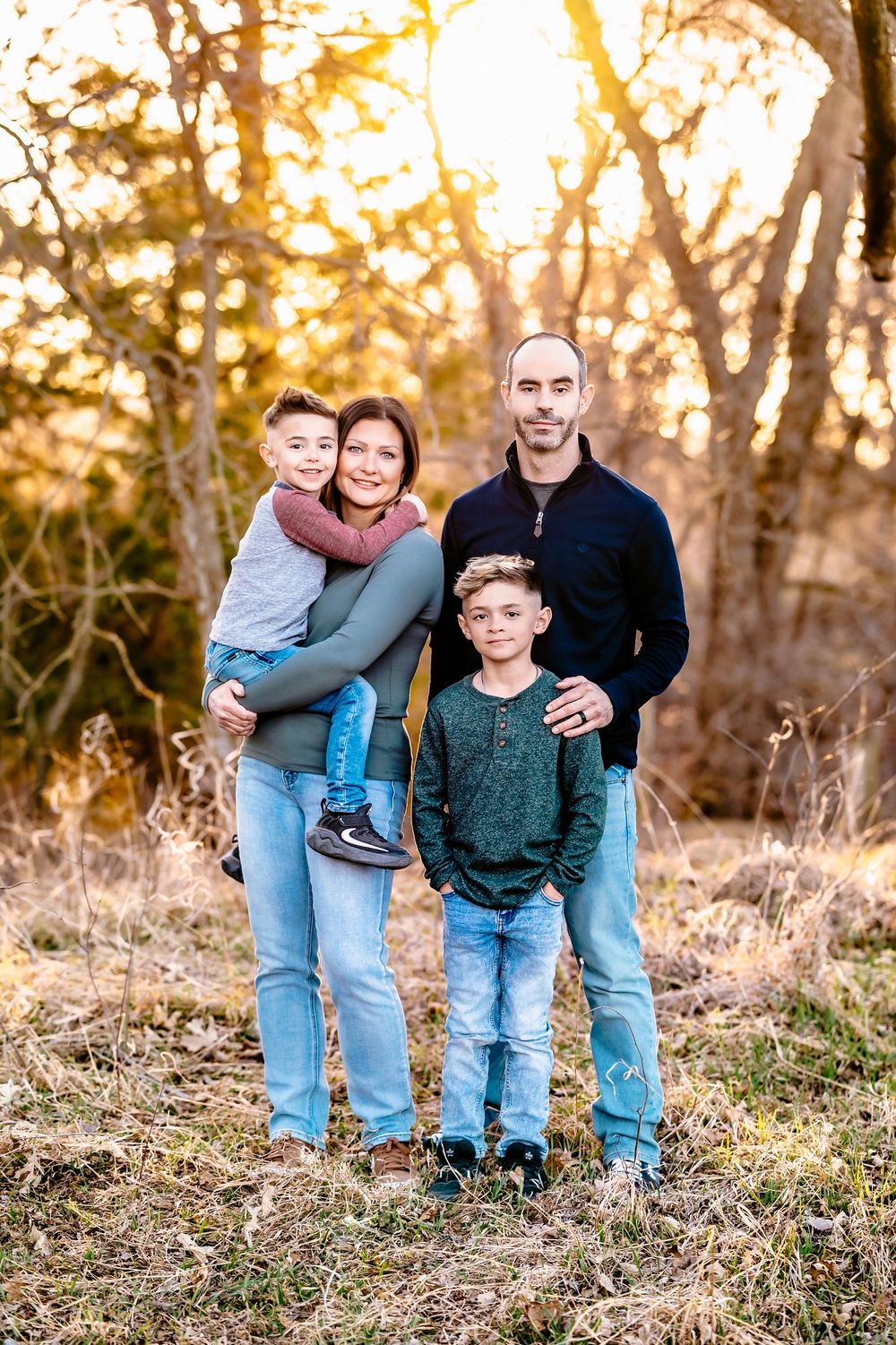 A family poses together outdoors during golden hour sunset with warm autumn lighting.