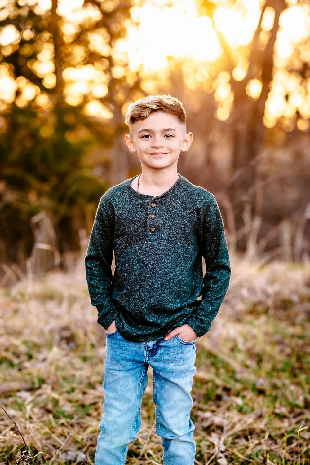 Youth wearing blue jeans and dark knit sweater poses outdoors at sunset with golden bokeh background.