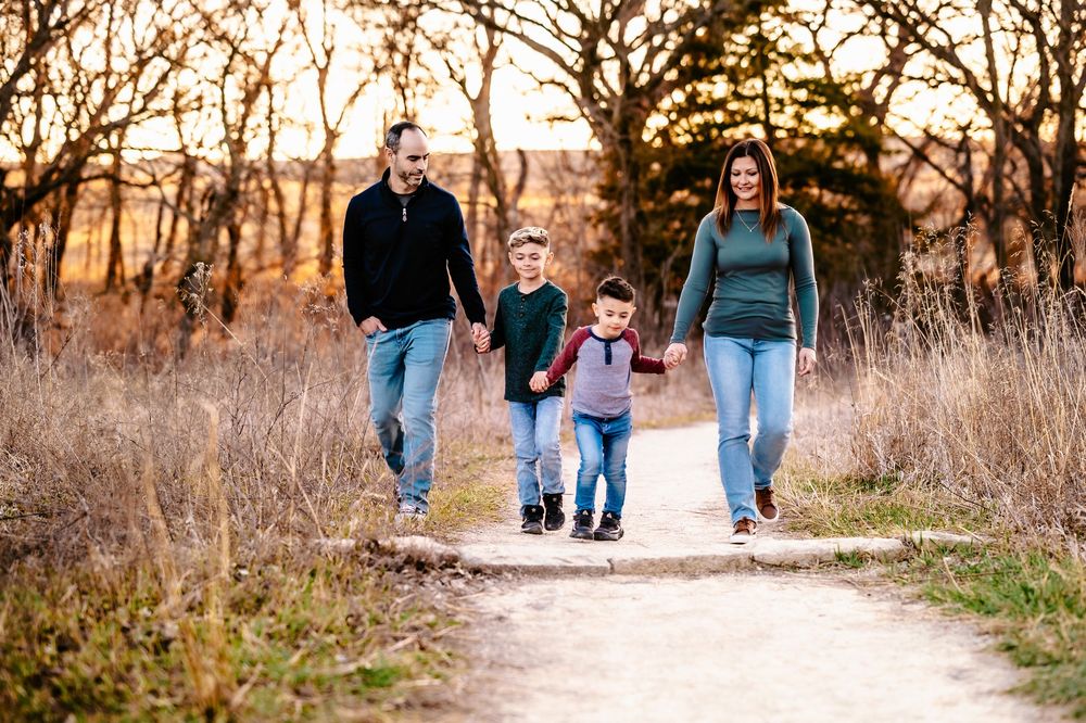 Family walking together on a nature trail path at sunset through tall grass and trees.