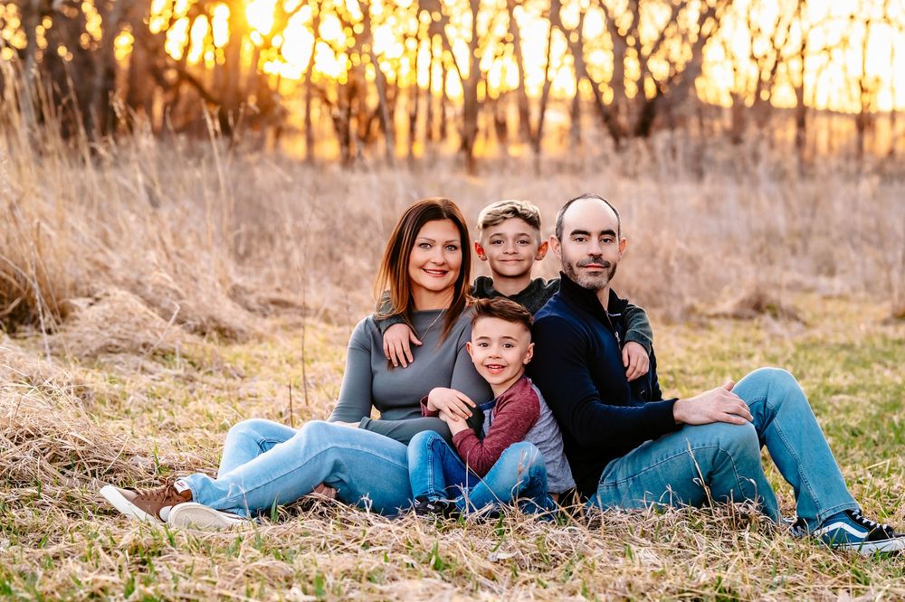A family relaxes together in a field at sunset with golden autumn light filtering through trees.