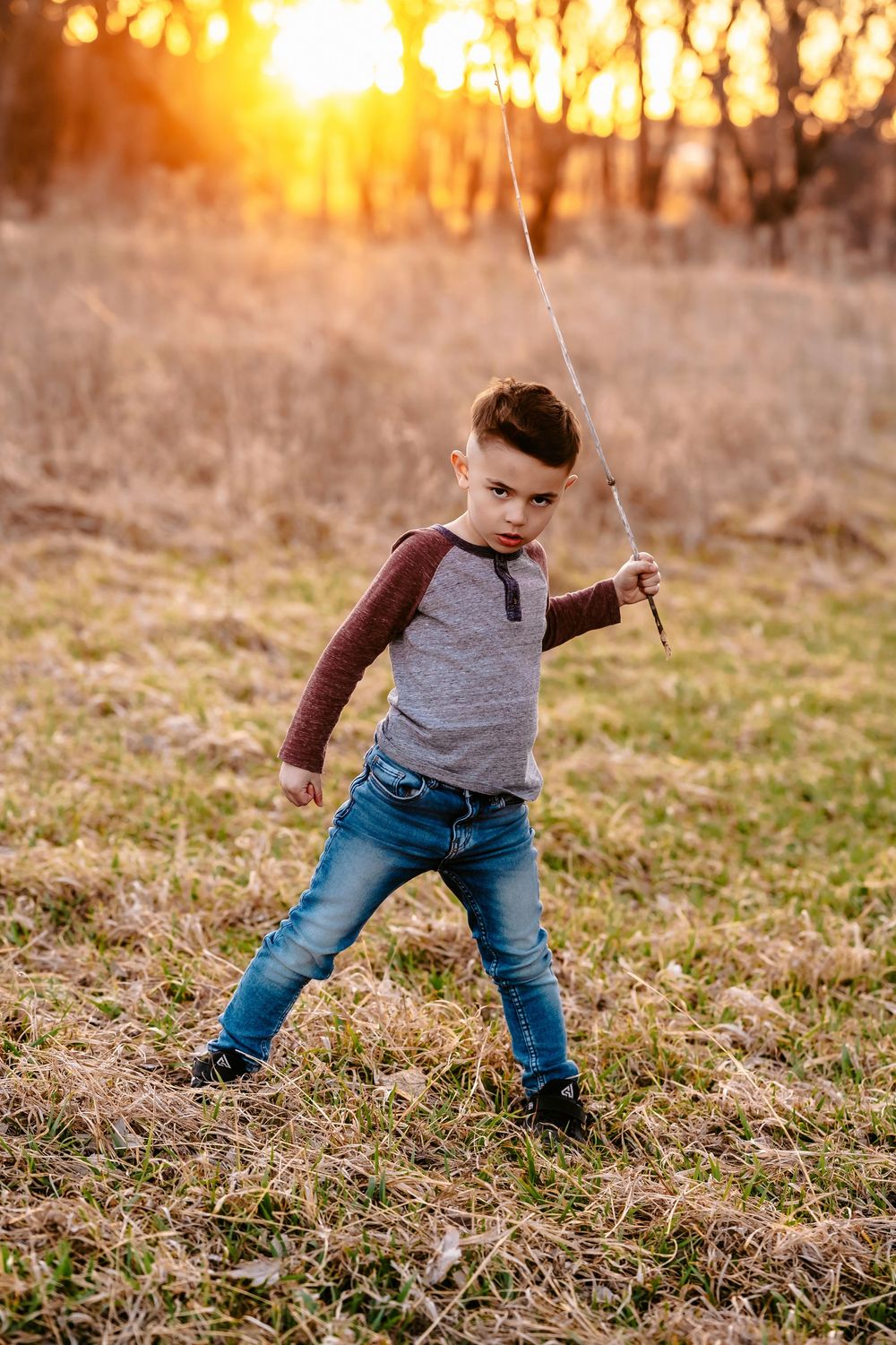 A child plays with a stick in a sun-drenched field during golden hour at sunset.