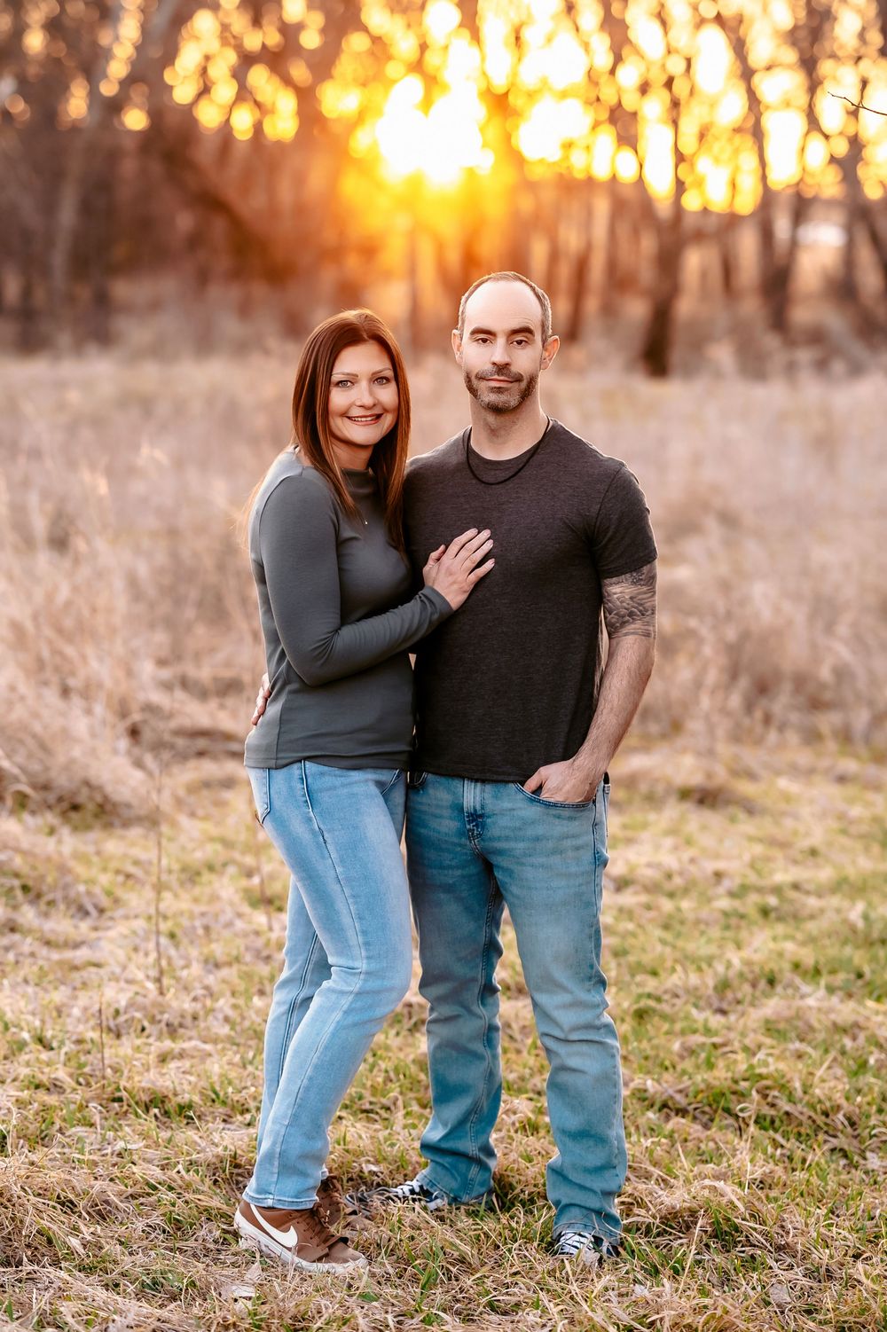 A couple embraces while standing in a sun-lit field during golden hour.