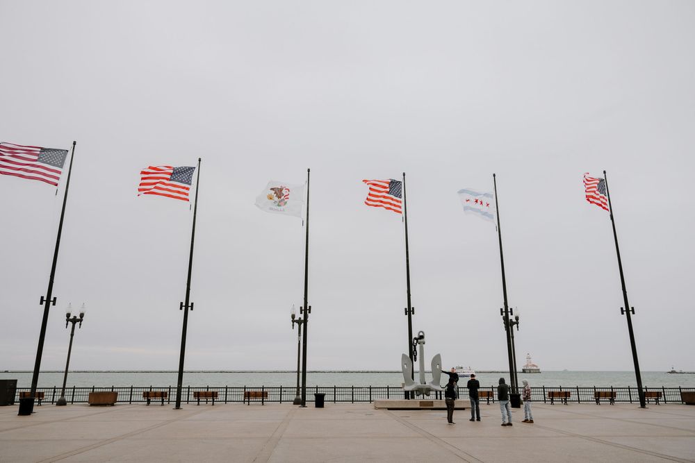 Several American flags wave in the wind along a misty waterfront pier with gray skies in the background.