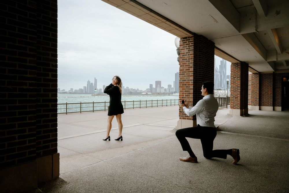 A surprise marriage proposal moment unfolds under a covered walkway with the Chicago skyline visible across the water.