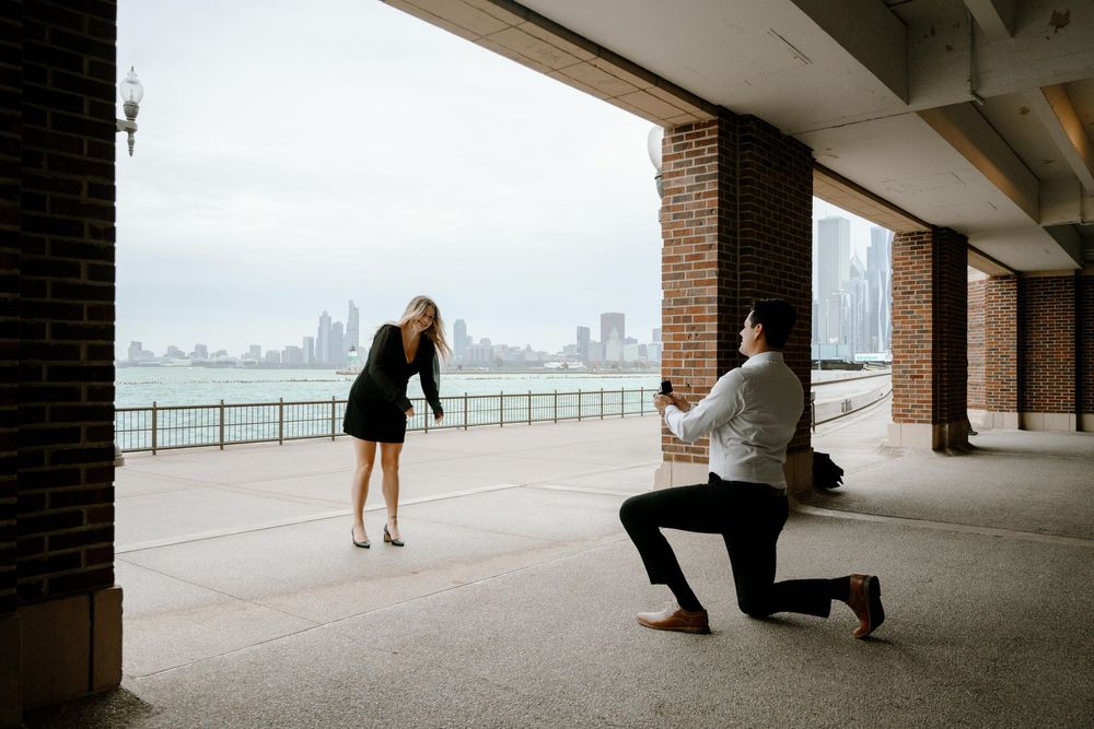 A proposal moment captured under a columned walkway with the Chicago skyline visible across Lake Michigan in the background.