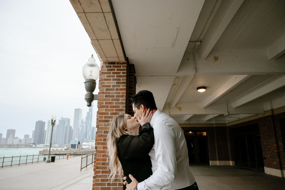 Two people share an intimate moment under a covered walkway with the Chicago skyline visible in the background.