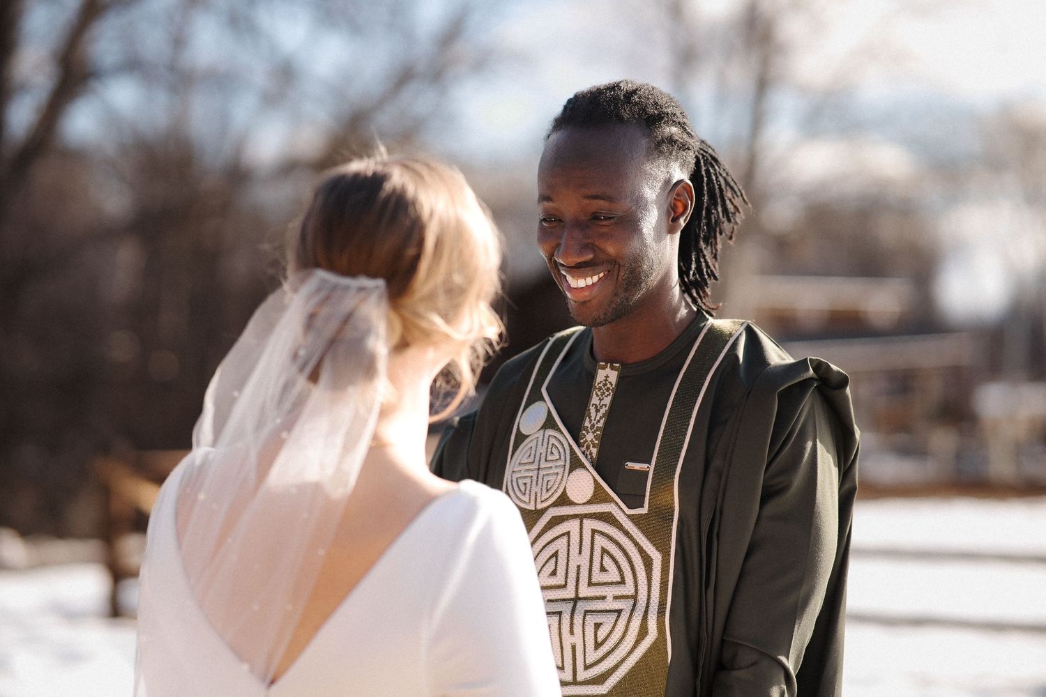 Two people share a joyful moment outdoors on a sunny winter day with one wearing a white veil.