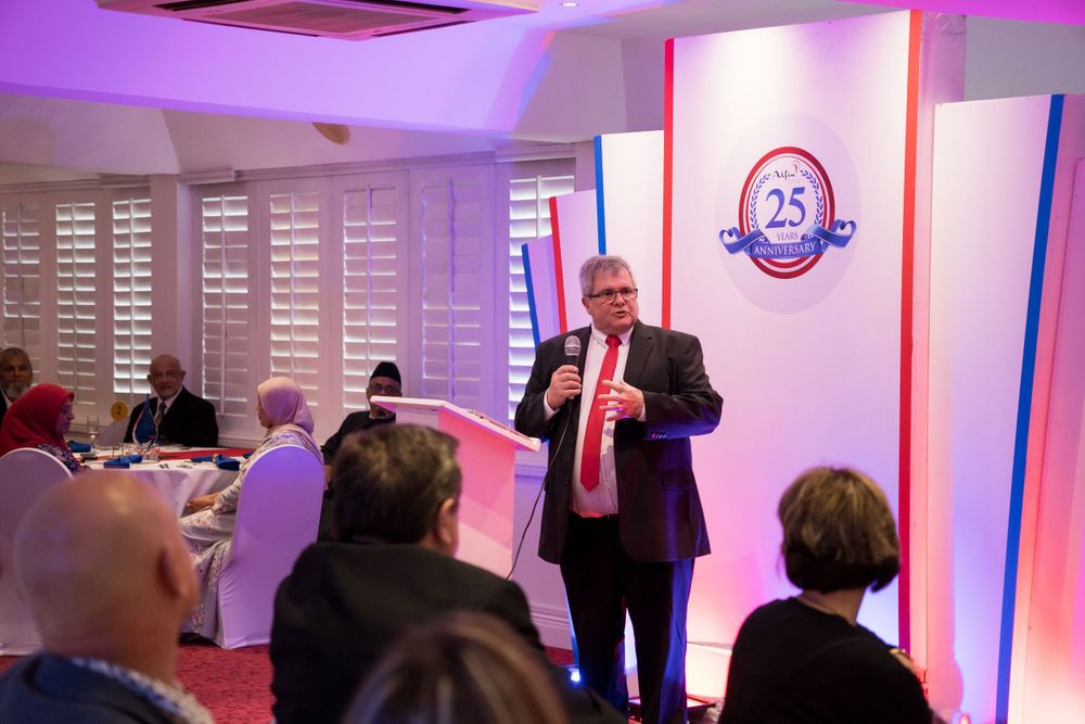 Speaker presenting at a corporate event with purple lighting and audience.