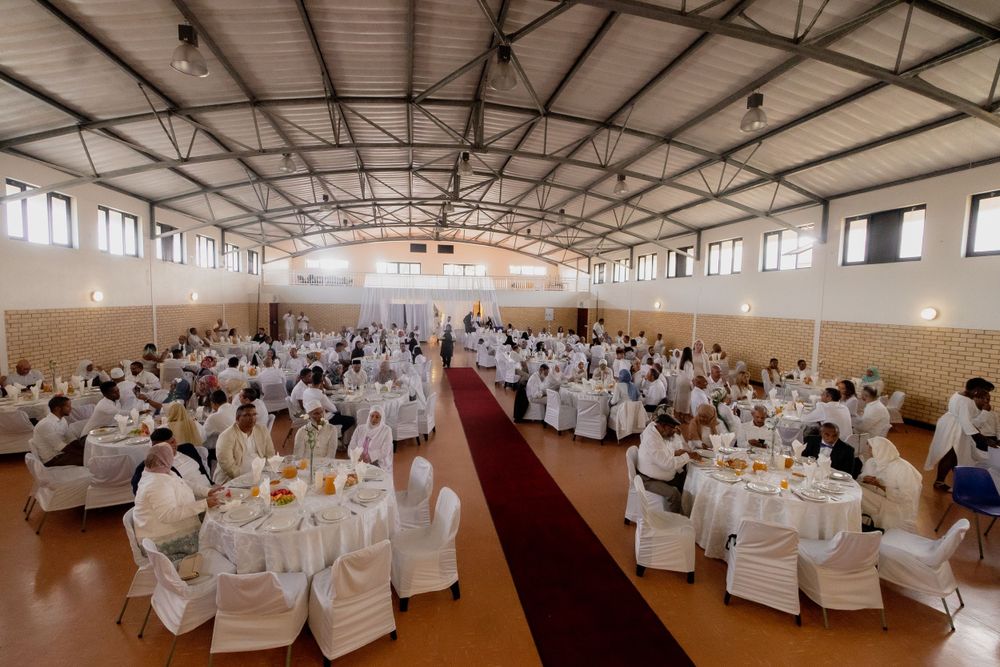 Large banquet hall decorated with white chair covers and round tables for formal event.
