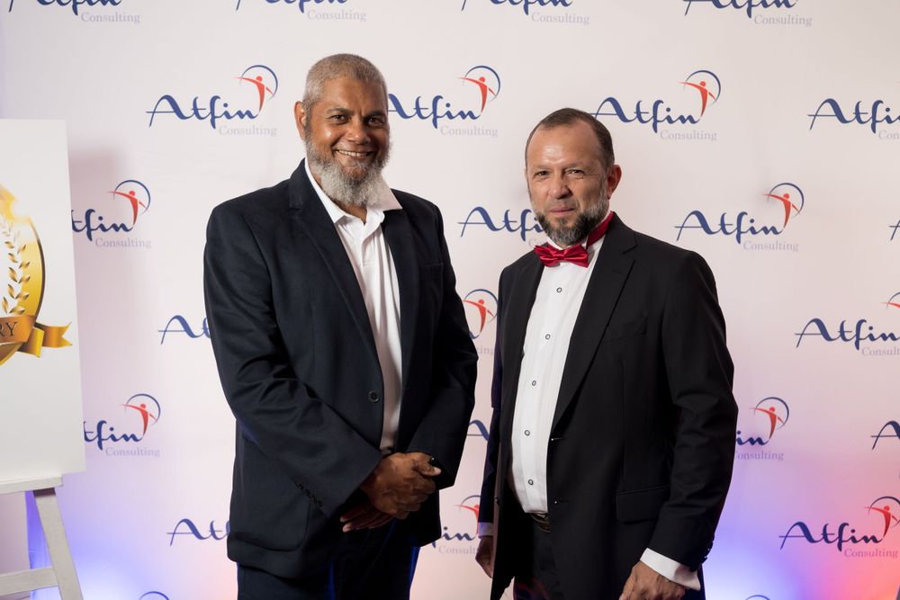 Two people posing at formal event with Alfa logo backdrop.